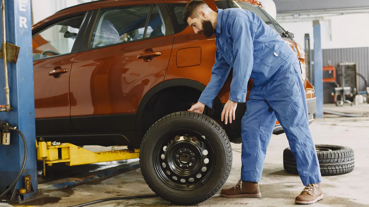 A car up on a two-post lift in a workshop with a wheel off.